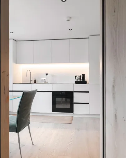 Moderne, voll ausgestattete Küche in einem Apartment des Aparthotel Hubertus in Mellau – mit weißen Fronten, integriertem Ofen und stilvoller Beleuchtung, perfekt für die Selbstversorgung während Ihres Aufenthalts im Bregenzerwald.