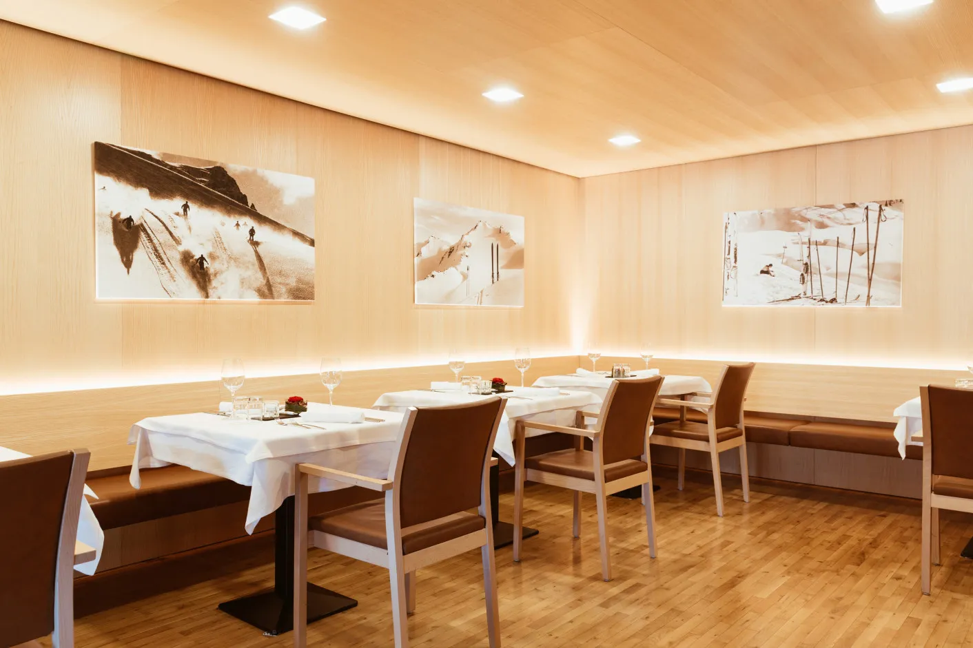 Einladendes Restaurant des Aparthotel Hubertus in Mellau, gestaltet mit hellem Holz und geschmückt mit großformatigen Bildern von Skiszenen – ein perfekter Ort, um die alpine Atmosphäre und die exquisite Küche im Bregenzerwald zu genießen.