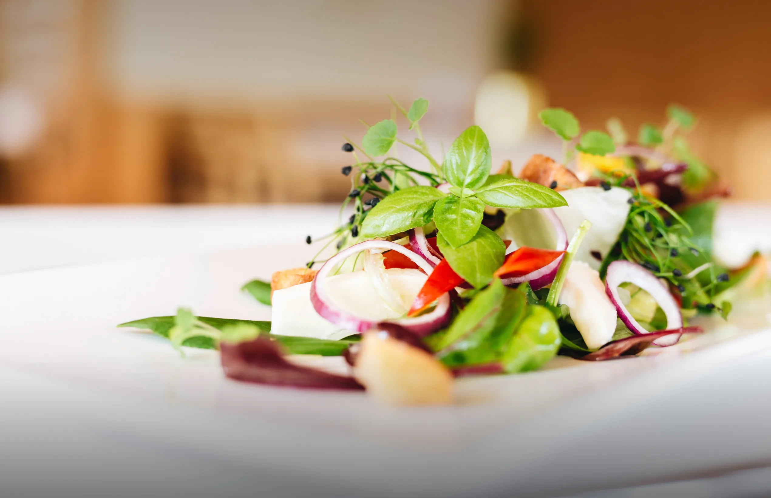 Ein kunstvoll angerichteter, frischer alpiner Salatteller mit bunten Zutaten, präsentiert auf einem weißen Tisch – symbolisiert die gesunde und regionale Kulinarik im Restaurant des Aparthotel Hubertus in Mellau, Bregenzerwald.