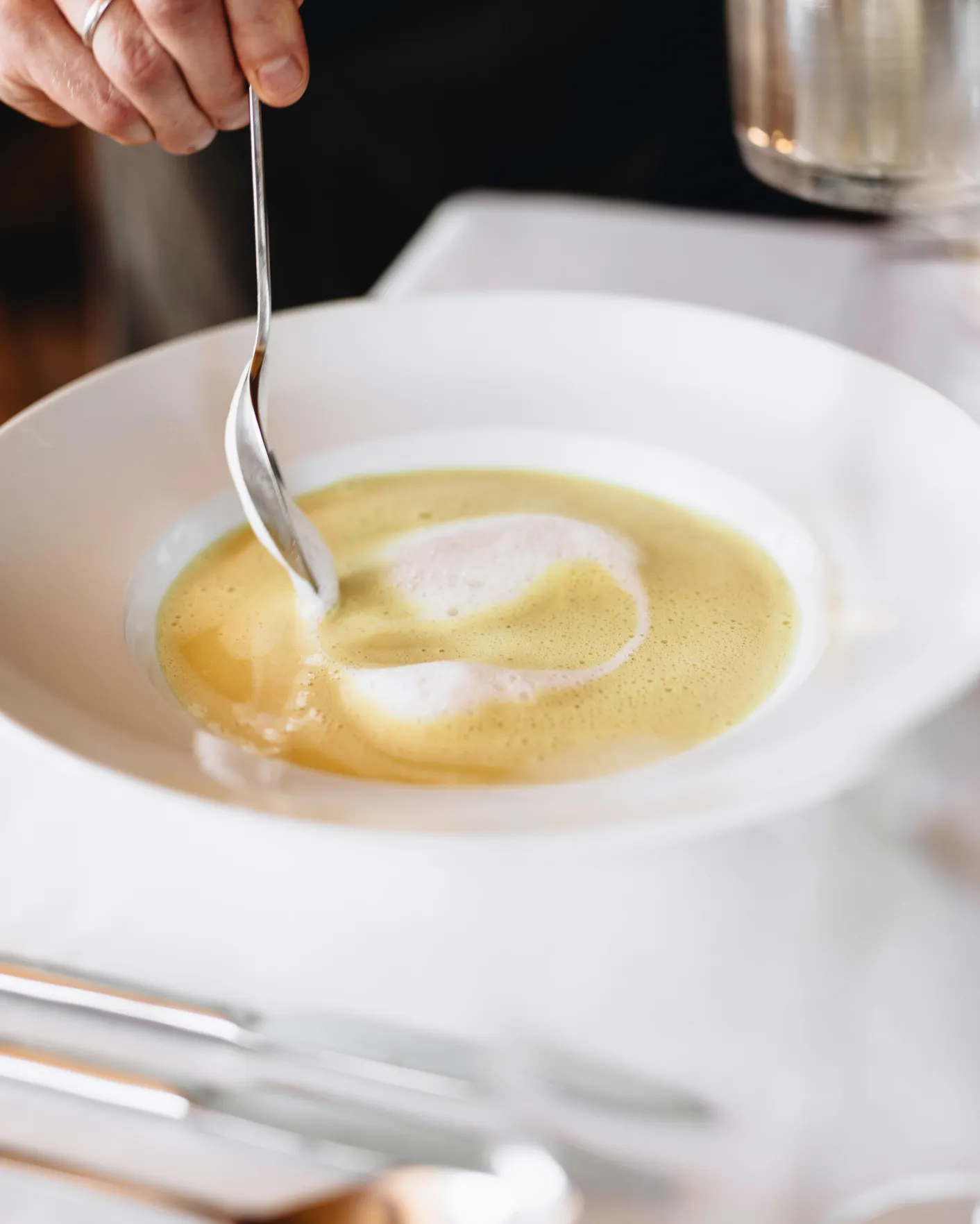 Nahaufnahme einer frisch zubereiteten, cremigen Suppe in einer weißen Schale, die mit einem Löffel gerührt wird – veranschaulicht die feine Kulinarik und den Genuss regionaler Speisen im Aparthotel Hubertus oder Berghaus Kanisfluh in Mellau.
