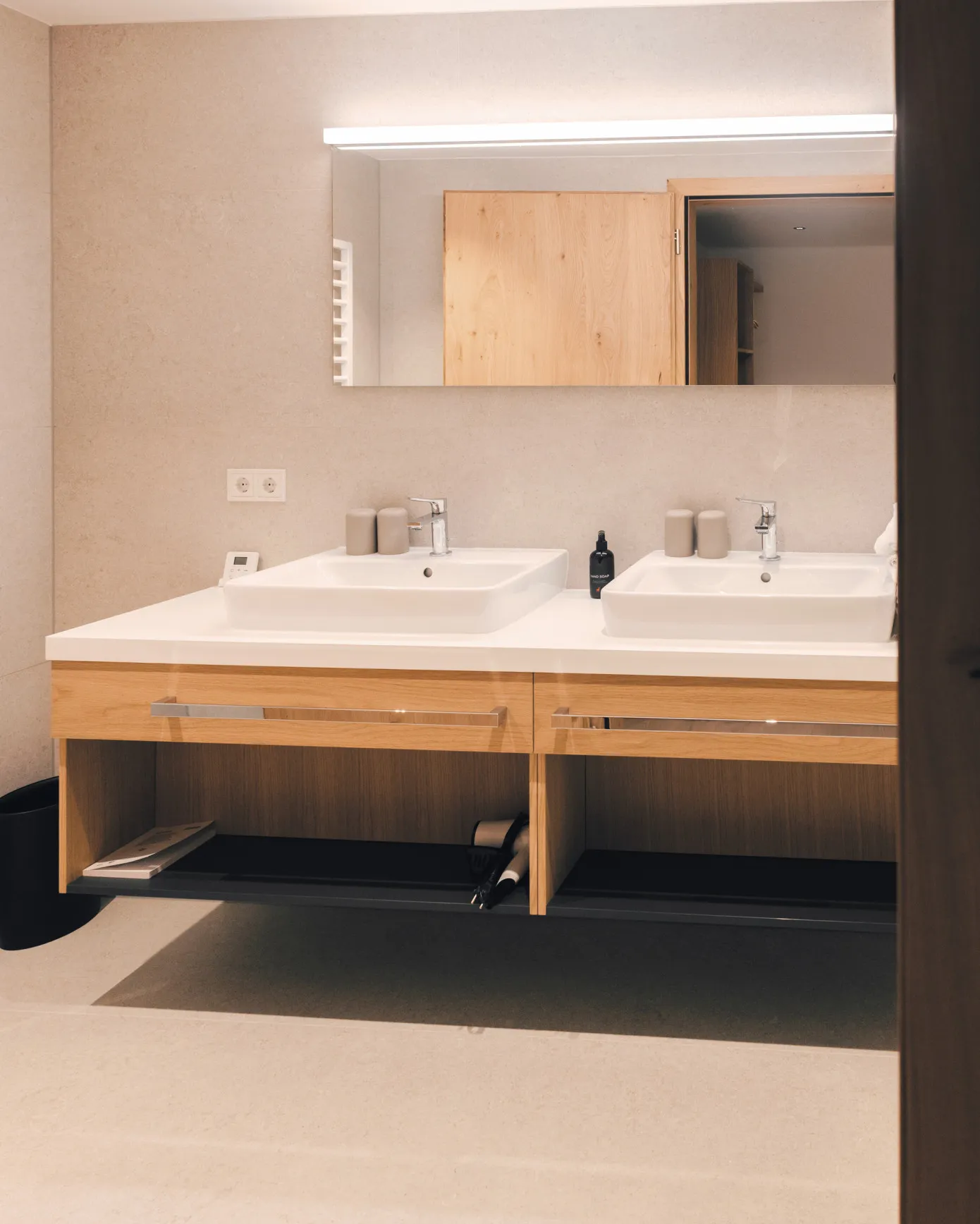Geräumiges Doppelwaschbecken im modernen Badezimmer eines Apartments im Aparthotel Hubertus in Mellau – mit zwei eleganten Waschbecken, großem Spiegel, Holzunterschrank und Handtuchwärmer, ideal für Komfort zu zweit im Bregenzerwald.