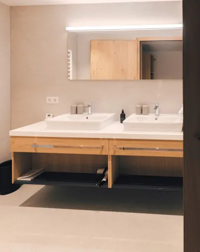 Geräumiges Doppelwaschbecken im modernen Badezimmer eines Apartments im Aparthotel Hubertus in Mellau – mit zwei eleganten Waschbecken, großem Spiegel, Holzunterschrank und Handtuchwärmer, ideal für Komfort zu zweit im Bregenzerwald.