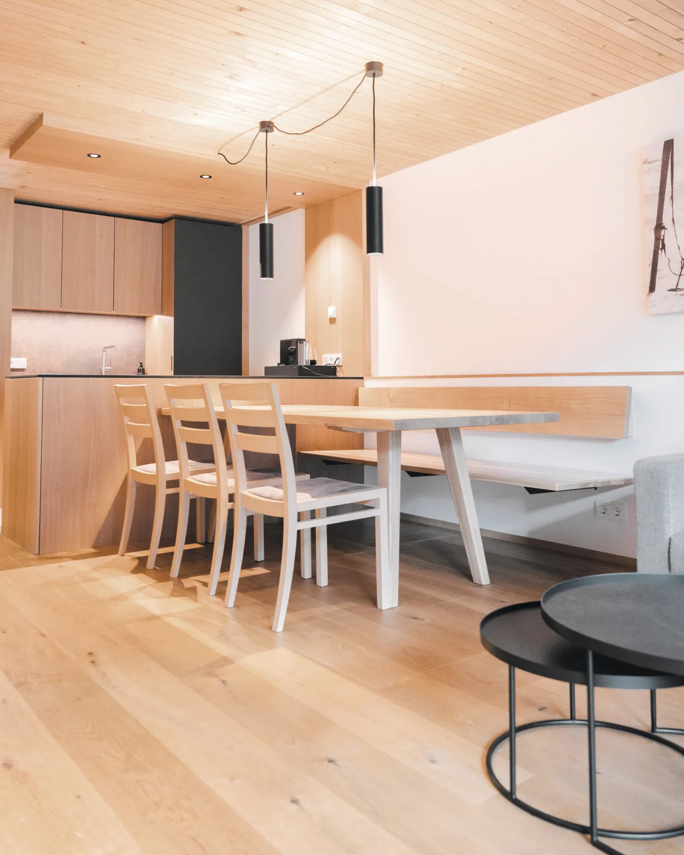 Geräumiger offener Wohn-, Ess- und Küchenbereich in einem Apartment des Aparthotel Hubertus in Mellau – zeigt die moderne Küche mit Holzfronten, einen Essbereich mit Holztisch und Bank sowie ein gemütliches Sofa mit Couchtischen, ideal für einen komfortablen Urlaub im Bregenzerwald.