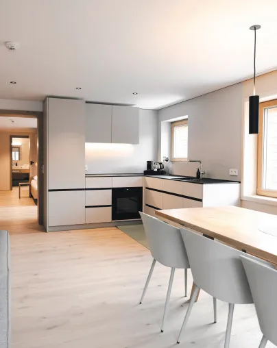 Moderner offener Küchen- und Essbereich in einem Apartment des Aparthotel Hubertus in Mellau – mit heller Einbauküche, Esstisch und Stühlen, ideal für Selbstversorger und mit direktem Zugang zu Schlaf- und Badezimmern, für einen komfortablen Aufenthalt im Bregenzerwald.