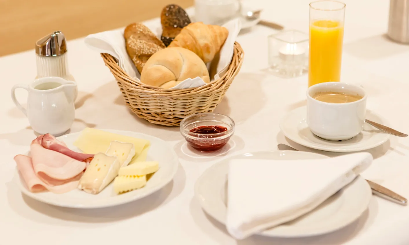 Ein reichhaltiges Frühstück im Aparthotel Hubertus in Mellau mit frischen Brötchen, Croissants, Käse- und Wurstplatte, Marmelade, Kaffee und Orangensaft – perfekt für einen genussvollen Start in den Tag im Bregenzerwald.