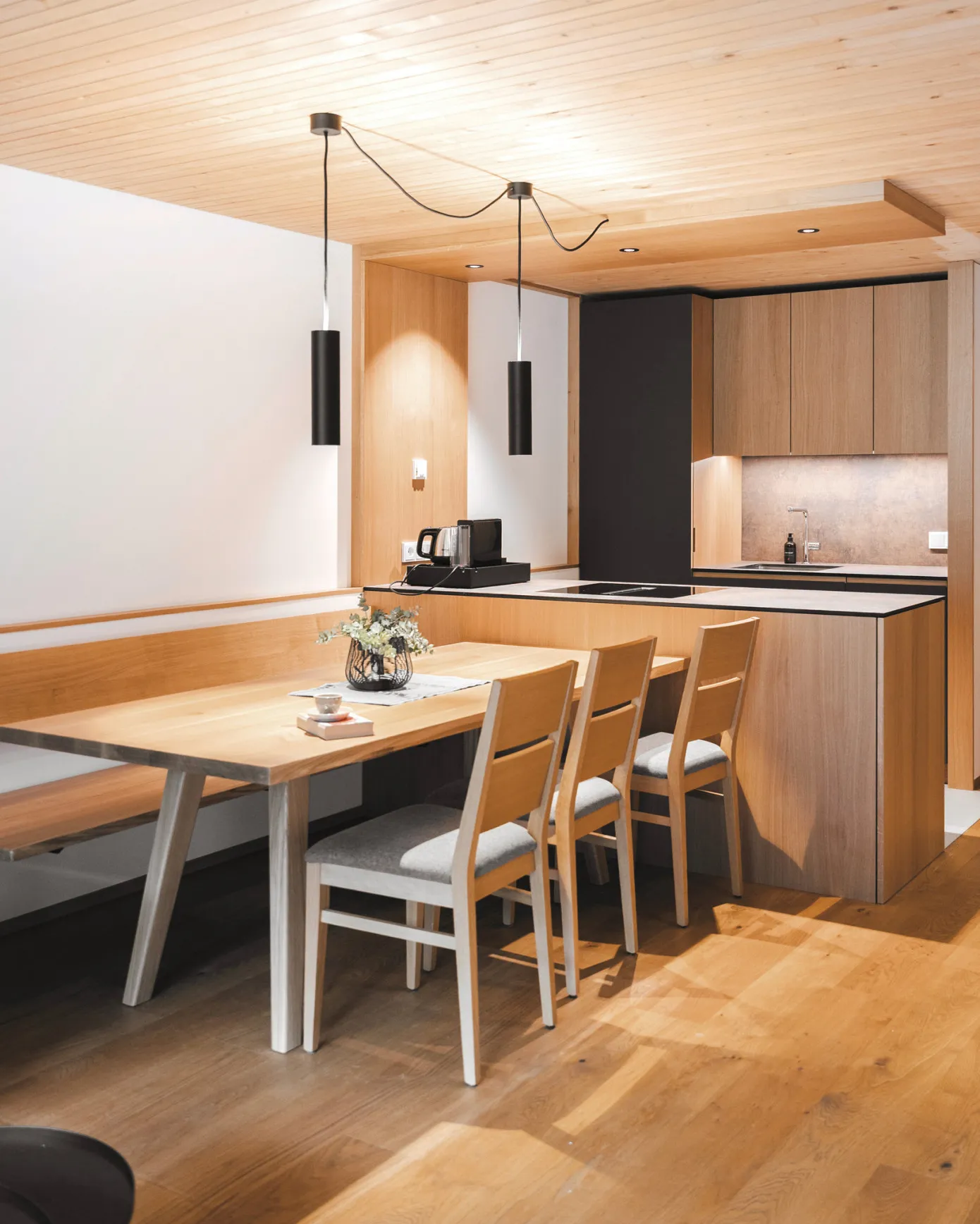 Moderner Essbereich mit Holztisch, Sitzbank und Stühlen sowie einer hochwertig ausgestatteten, integrierten Küche in einem Apartment des Aparthotel Hubertus in Mellau – ideal für gesellige Kochabende und gemütliche Stunden im Bregenzerwald.