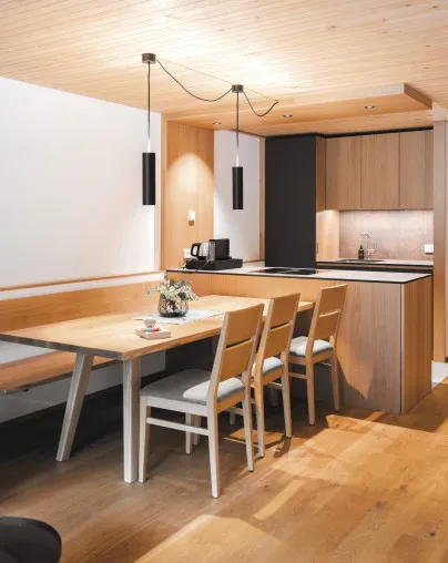 Moderner Essbereich mit Holztisch, Sitzbank und Stühlen sowie einer hochwertig ausgestatteten, integrierten Küche in einem Apartment des Aparthotel Hubertus in Mellau – ideal für gesellige Kochabende und gemütliche Stunden im Bregenzerwald.